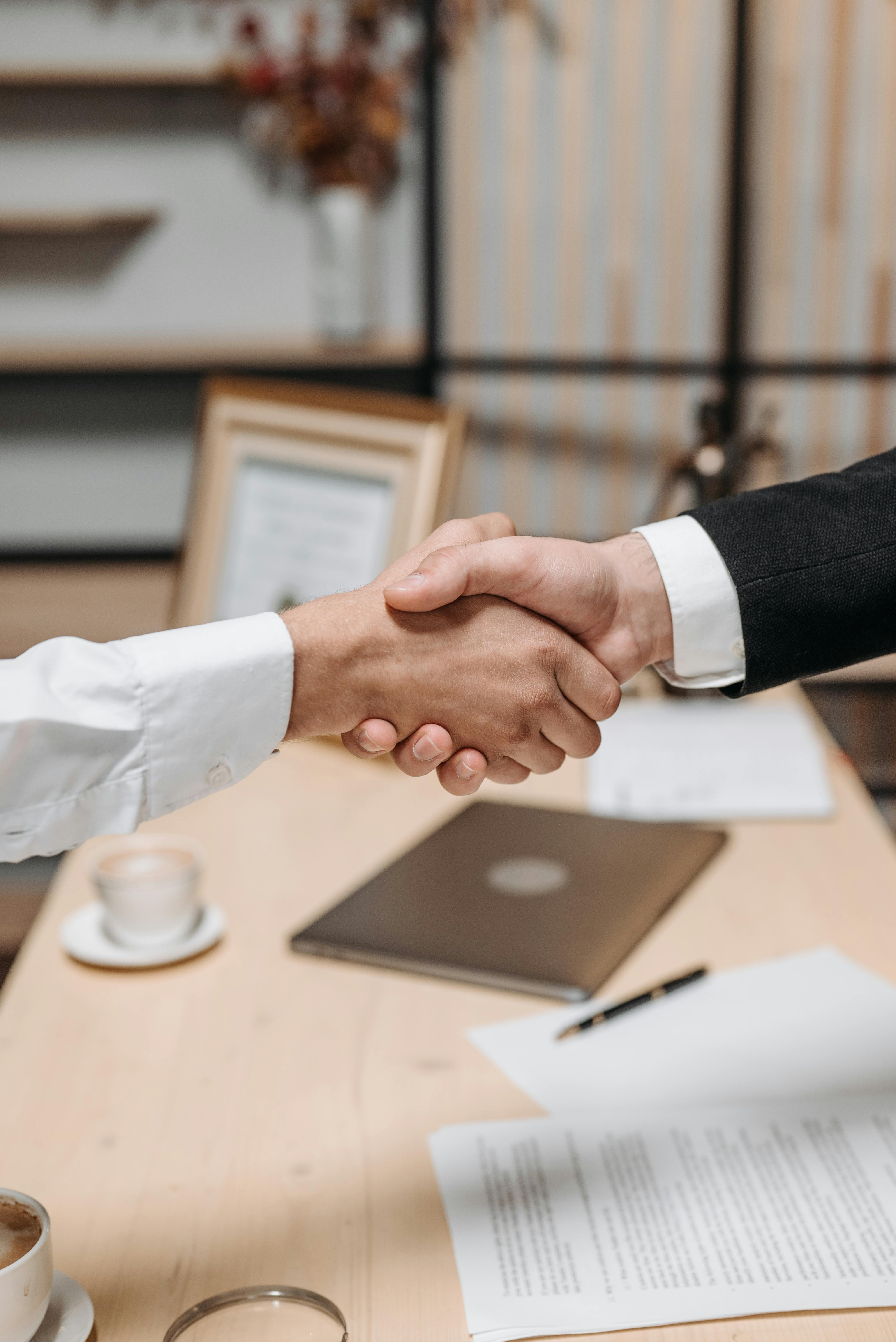 Deux professionnels se serrant la main au-dessus d’une table avec des documents et un ordinateur portable